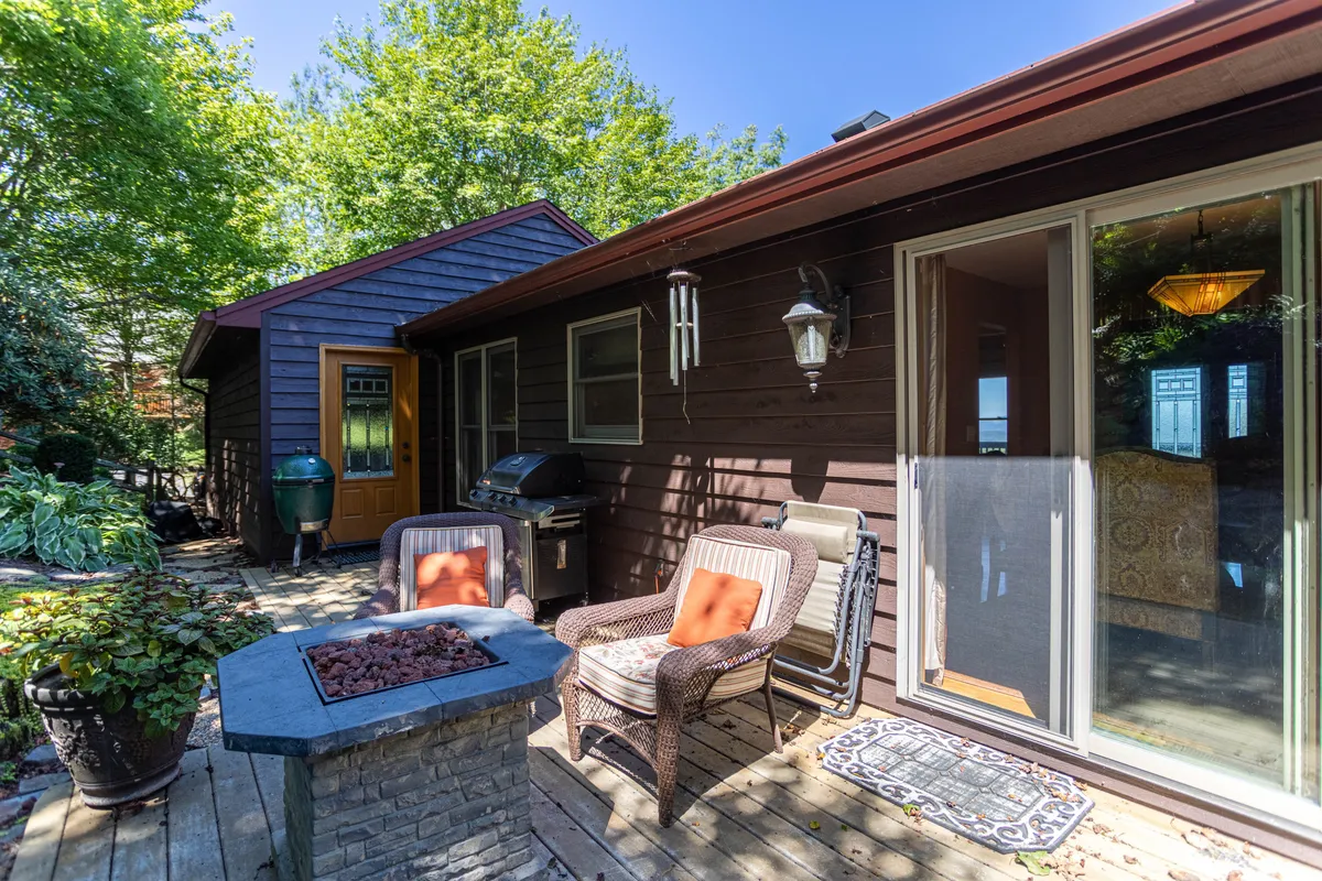A spacious wooden deck equipped with an outdoor seating area, fire pit, and grill, all set against a backdrop of greenery and open skies. The setup suggests gatherings around the fire, grilling meals, and enjoying the sunset from a comfortable vantage point.