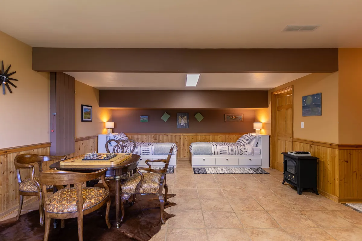 A cozy, inviting space featuring a dining table for games or casual meals, two twin beds cleverly integrated into the room, warm artwork on the walls, and a compact stove that hints at warmth and relaxation. The room is versatile, supporting both sleeping and active play, ideal for kids, teens, or family gatherings.