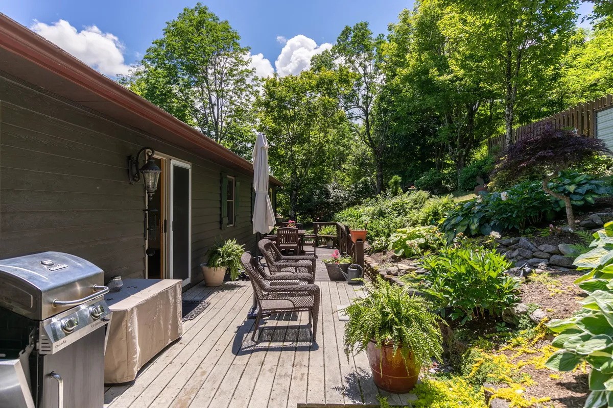 An exterior grilling area with ample seating, surrounded by vibrant greenery and a stone pathway. The space is set up for barbecuing and enjoying relaxed evenings, with room for socializing and soaking in the natural ambiance.