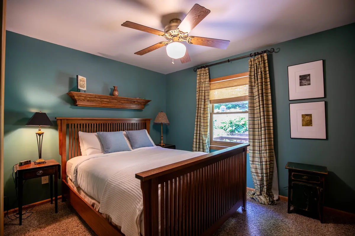 A peaceful bedroom with a neatly made bed, window that allows in natural light, a side table with lamp, and calming artwork. The setting feels restful and private, ideal for unwinding after a day of adventure.