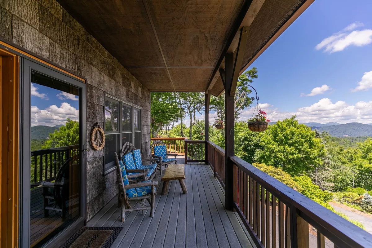 A peaceful exterior scene with comfortable chairs and a wooden table arranged for relaxation or socializing. The setting overlooks a mountain view and is complemented by potted flowers, suggesting beauty in every season—sunrises, star-gazing, and seasonal blooms.