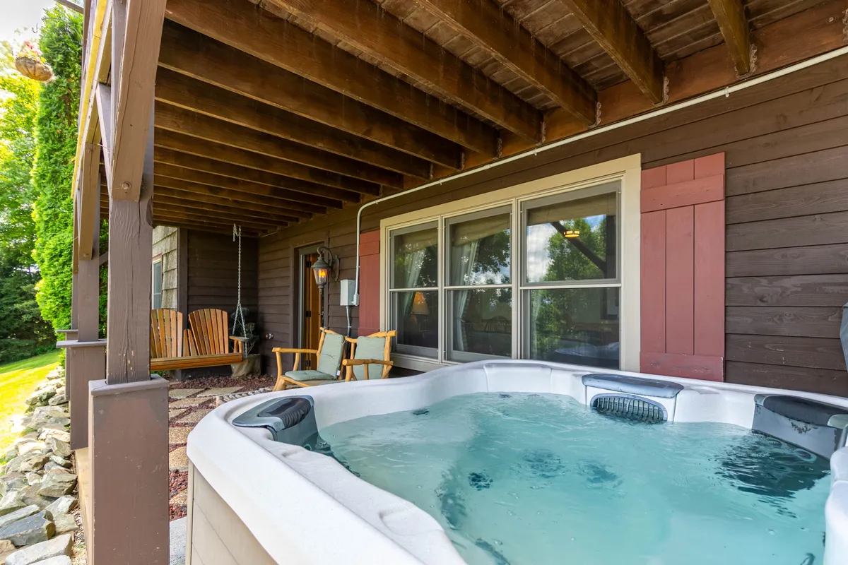 A cozy exterior shot featuring a hot tub and rocking chairs under wooden beams, all set against a natural backdrop. The space looks perfect for unwinding after a day on the slopes or trails, with plenty of fresh mountain air and views.