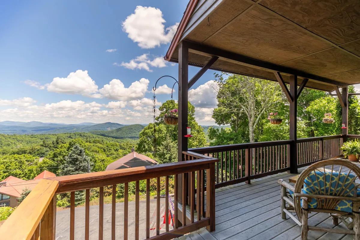 This image showcases a serene seating area on a deck, with a clear view of the mountains in the background. The deck railing, hanging plants, and cozy seating invite guests to step outside and enjoy the surroundings. The atmosphere is peaceful and encourages relaxation while taking in the expansive natural beauty.
