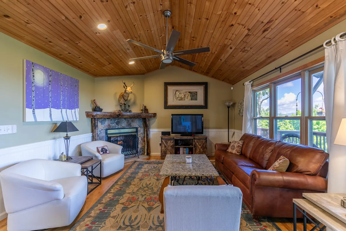A living area with a leather sofa, prominent stone fireplace, wooden ceiling, and stylish artwork, creating a warm and comfortable environment for movie nights or après-ski relaxation with family and friends.